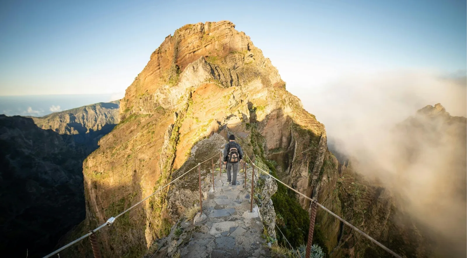 A hiker on the stone PR1 stairway with cloud spilling over the ridge