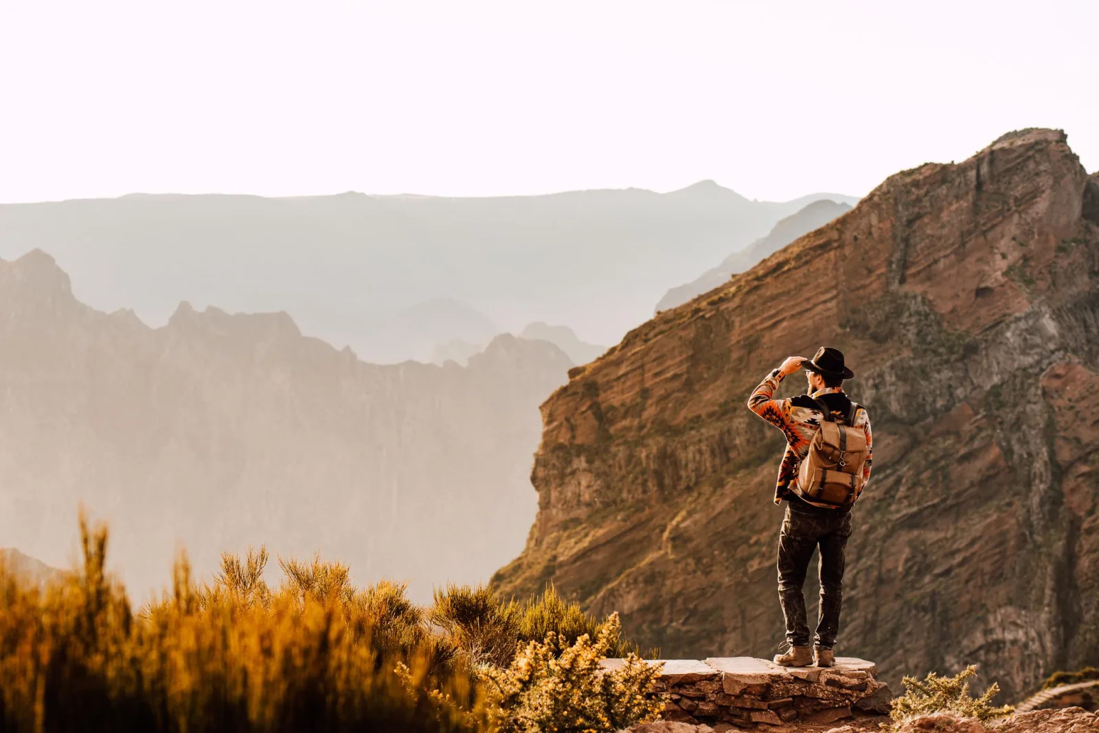 A hiker looking out from the ridge over layered mountain silhouettes at dawn